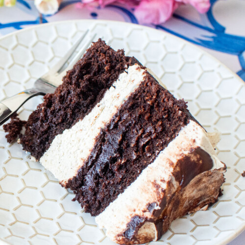 vegan sweet potato chocolate cake slice on a plate on a blue tile table with fresh flowers.