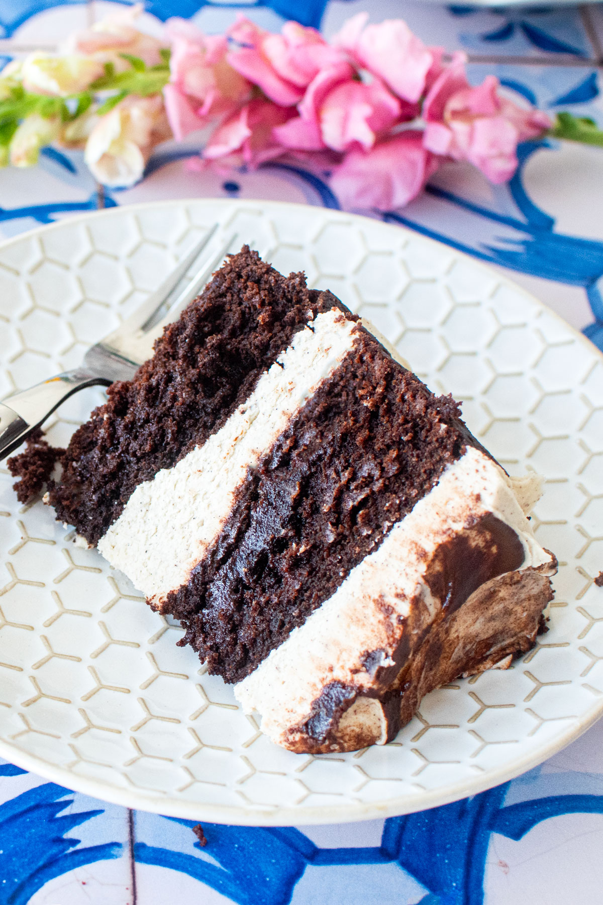 vegan sweet potato chocolate cake slice on a plate on a blue tile table with fresh flowers.