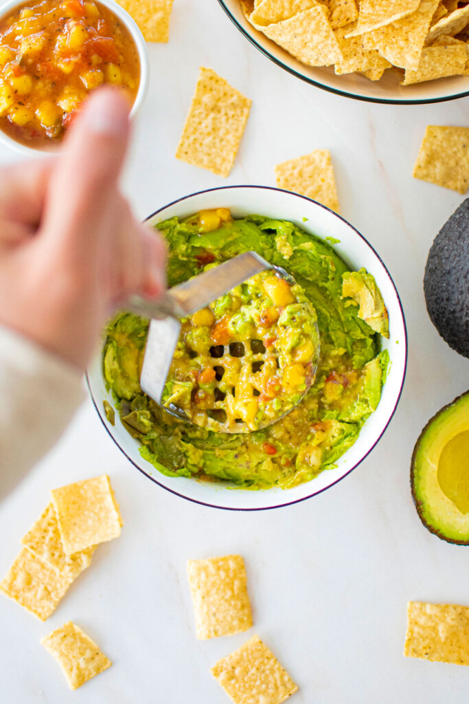 mango guacamole being mashed in a bowl with a potato masher.
