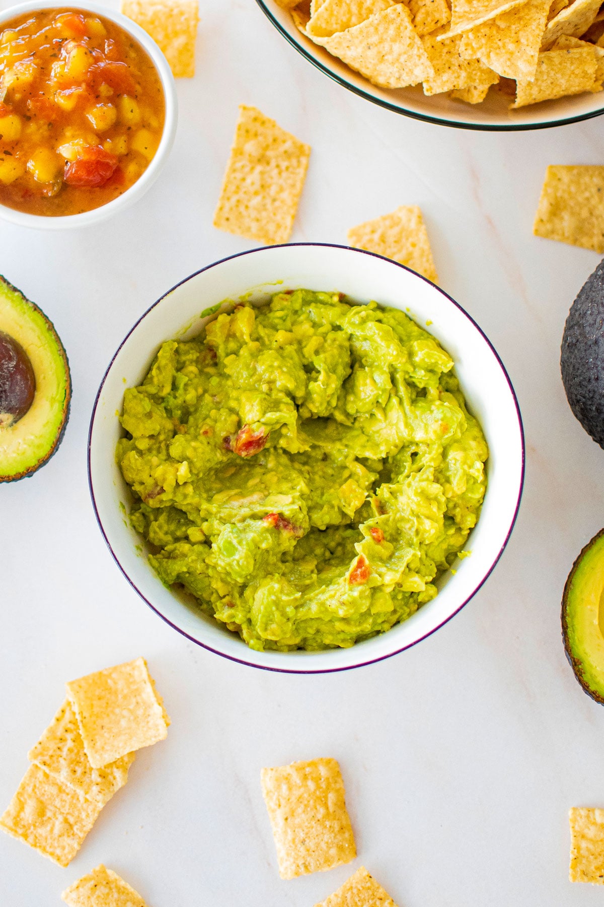 3 ingredient mango guacamole in a bowl on a marble counter with chipps and avocado.