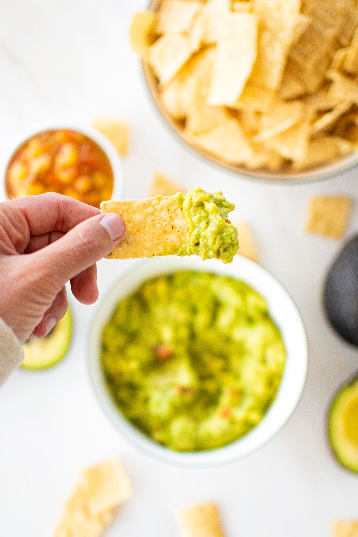 chip dipped into a bowl of mango guacamole on a marble countertop.