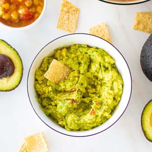 3 ingredient mango guacamole in a bowl on a marble counter with chipps and avocado.