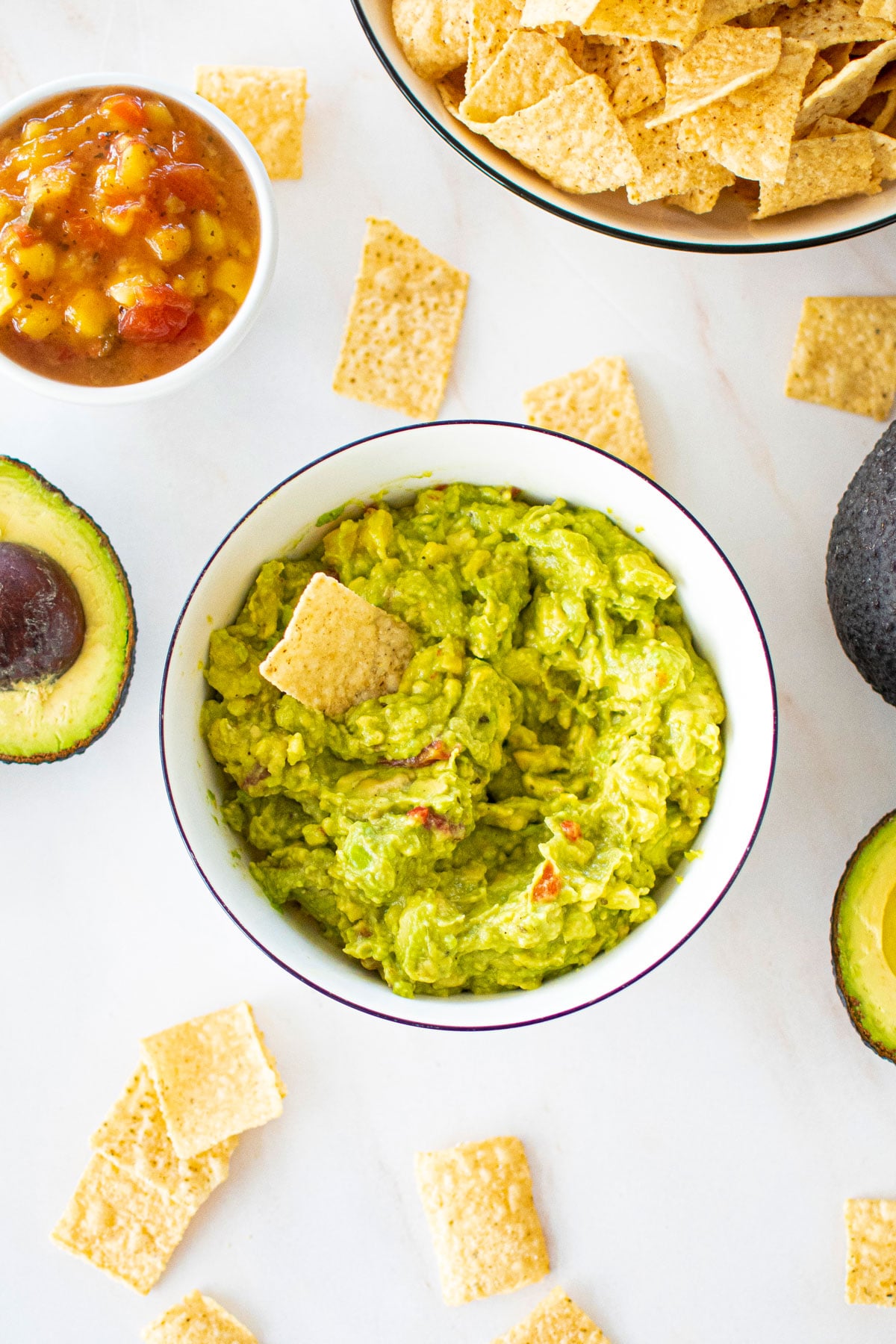 3 ingredient mango guacamole in a bowl on a marble counter with chipps and avocado.
