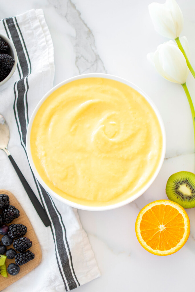 mango smoothie in a white bowl on a white marble countertop.