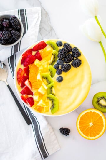 rainbow smoothie bowl on a white marble countertop with fresh fruit around.