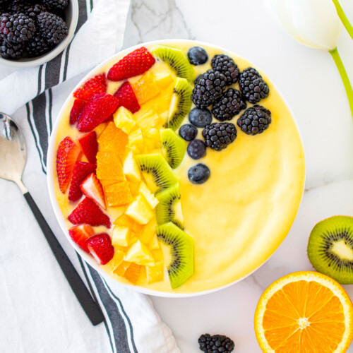 rainbow smoothie bowl on a white marble countertop with fresh fruit around.