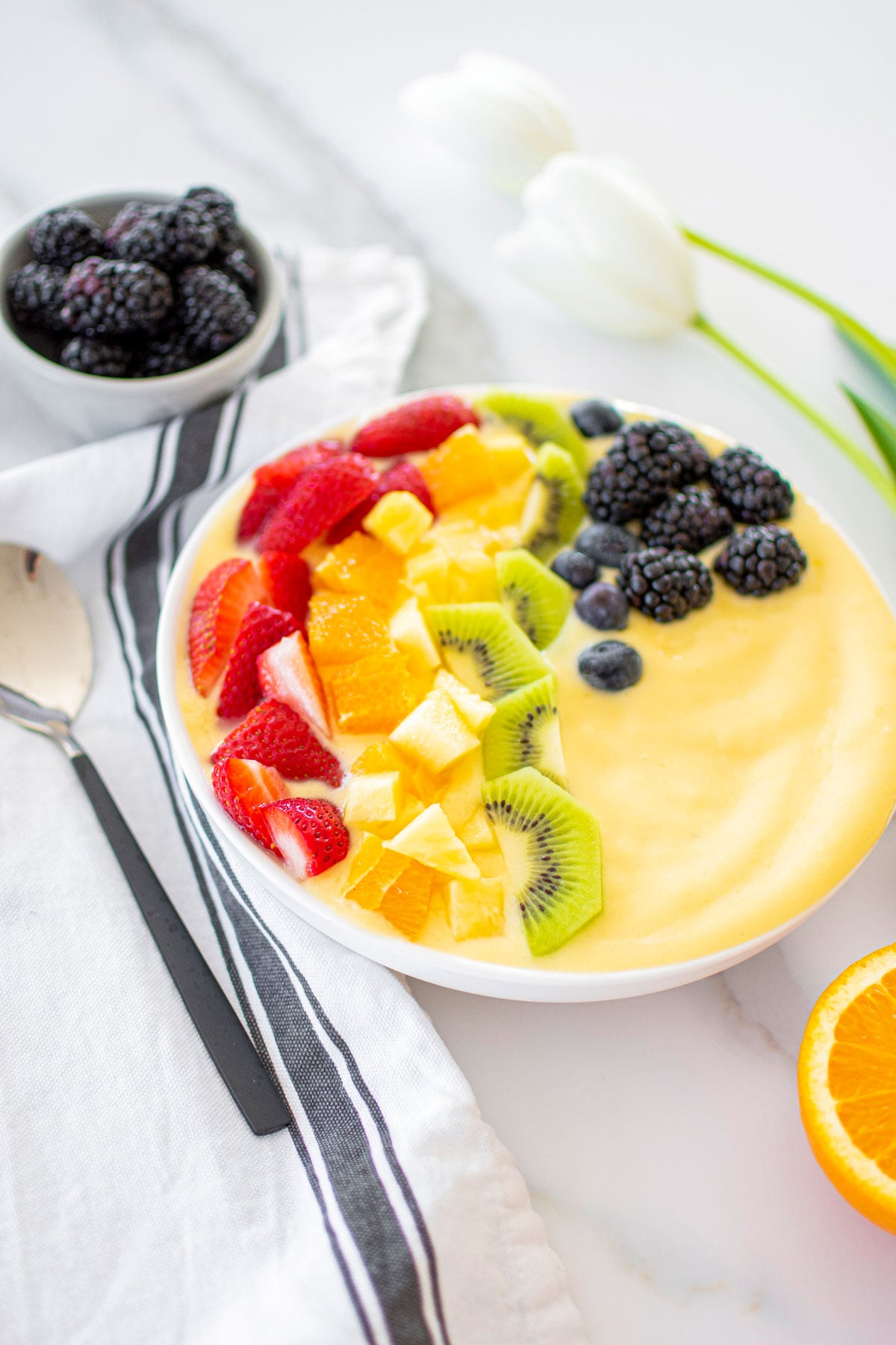 rainbow smoothie bowl on a white marble countertop with fresh fruit around.