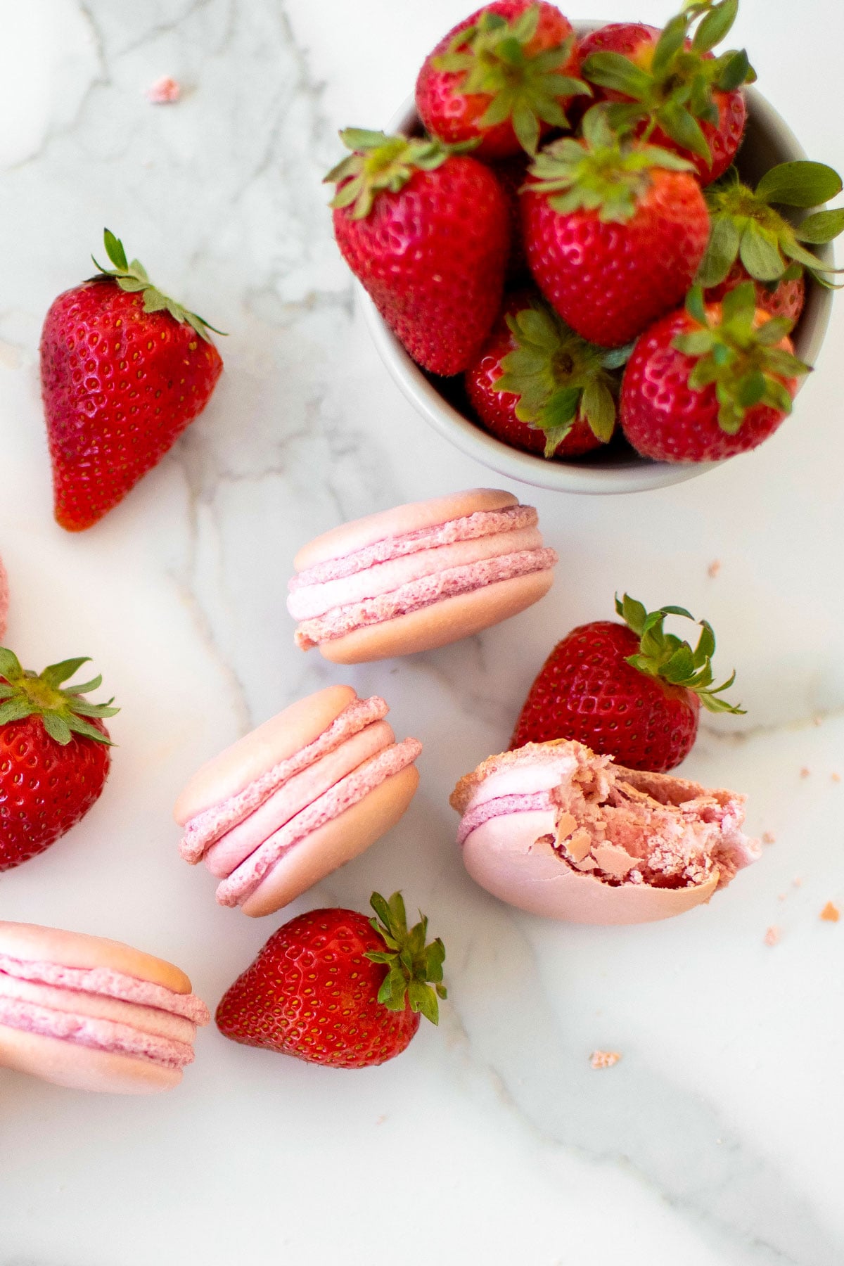 strawberry french macarons on a marble counter with fresh strawberries.