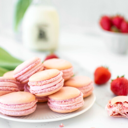 plate of strawberry french macarons on a marble counter with fresh strawberries.