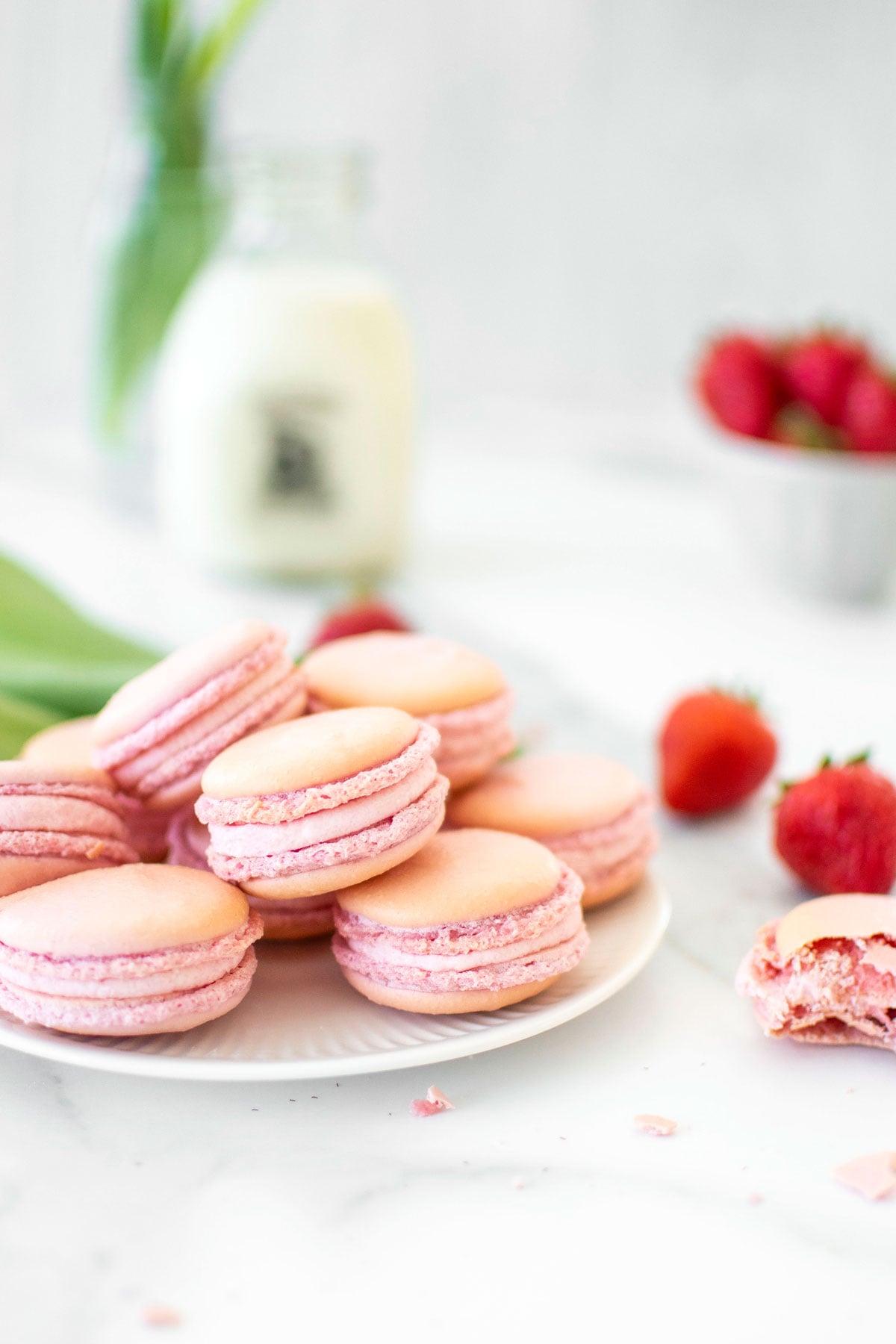 plate of strawberry french macarons on a marble counter with fresh strawberries.