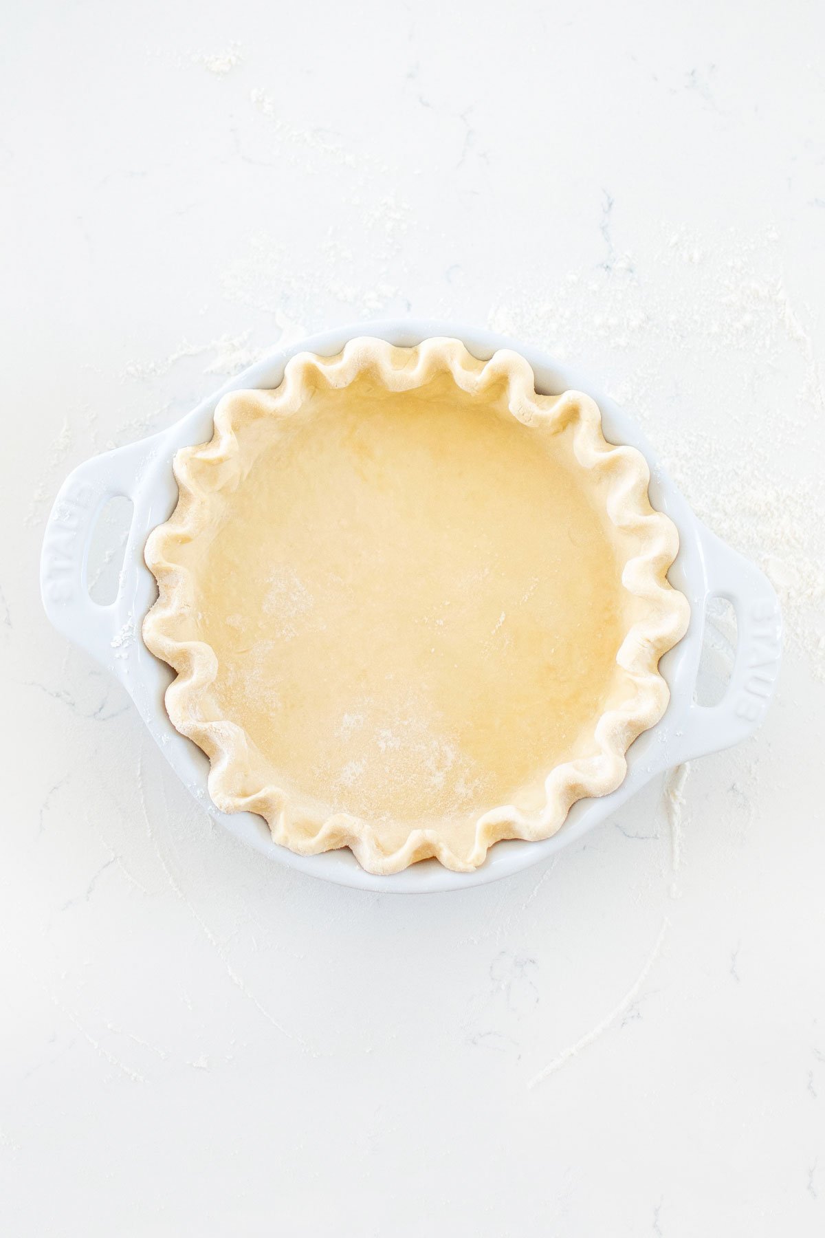 all butter pie crust in a white ceramic pie dish on a marble counter.