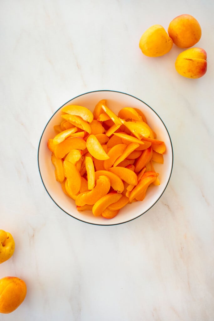 large bowl of sliced apricots on a marble counter.