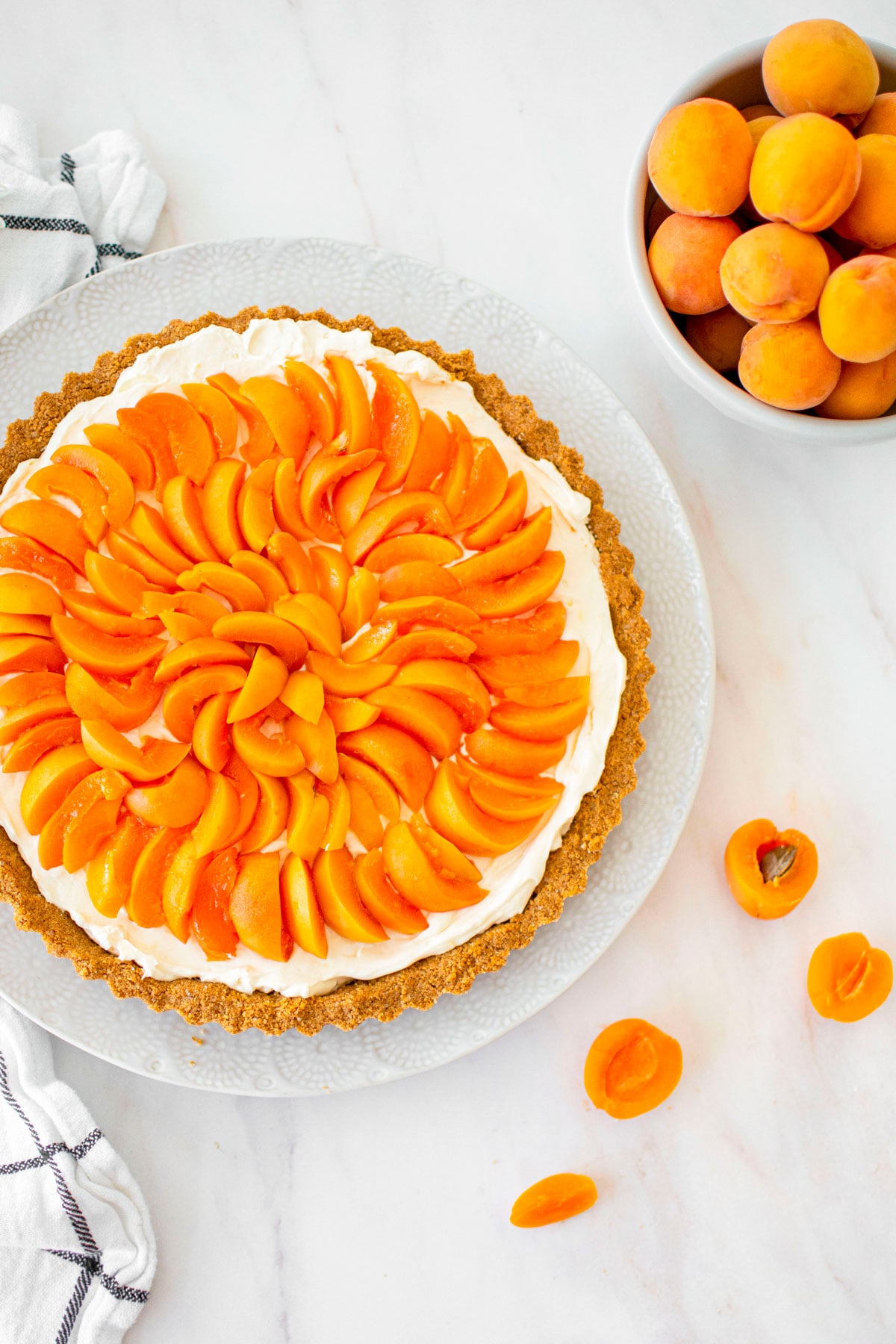 apricot cheesecake tart on a plate on a marble table with fresh flowers and apricots.