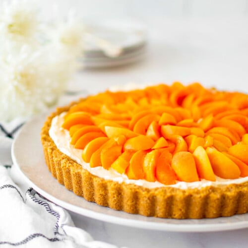 apricot cheesecake tart on a plate on a marble table with fresh flowers.
