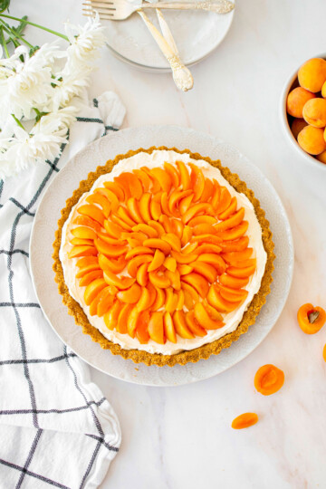 apricot cheesecake tart on a plate on a marble table with fresh flowers and apricots.