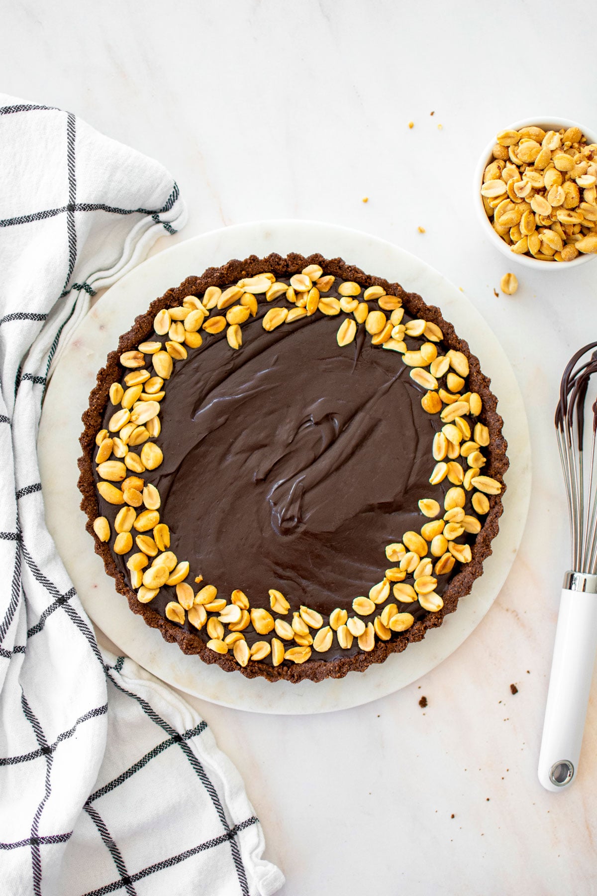 chocolate peanut butter tart with chocolate graham cracker crust and peanuts on top on a marble serving board.