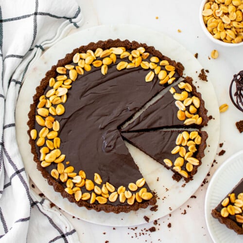 chocolate peanut butter tart with chocolate graham cracker crust cut into slices on a marble serving board.