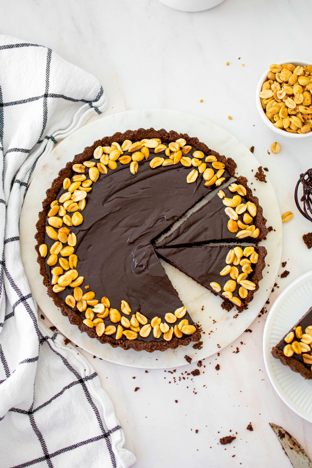 chocolate peanut butter tart with chocolate graham cracker crust cut into slices on a marble serving board.
