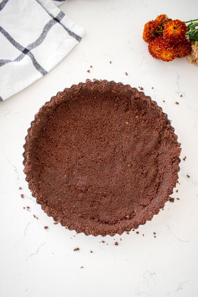 chocolate graham cracker crust pressed into a tart pan on a marble counter with fresh flowers.