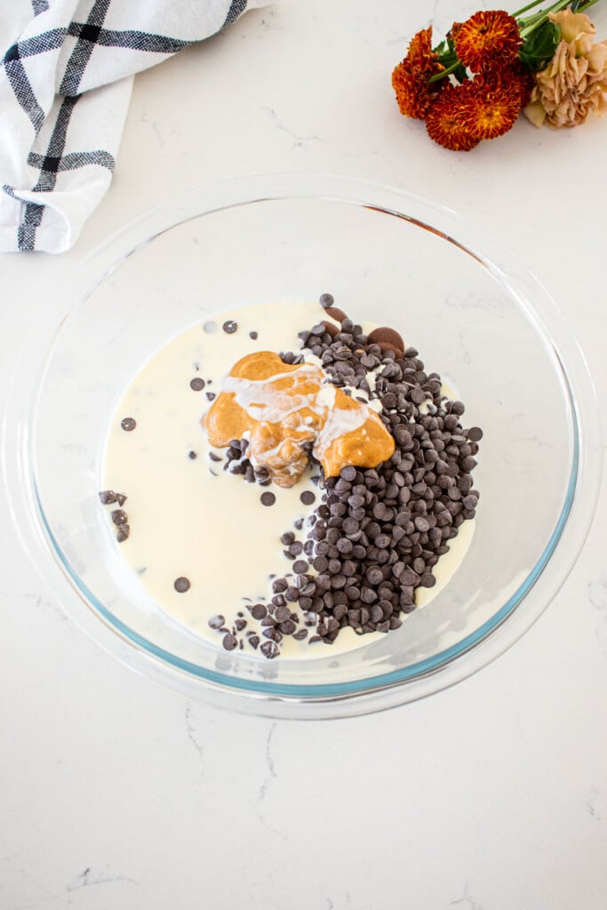 glass mixing bowl with chocolate, heavy cream and peanut butter on a marble countertop.