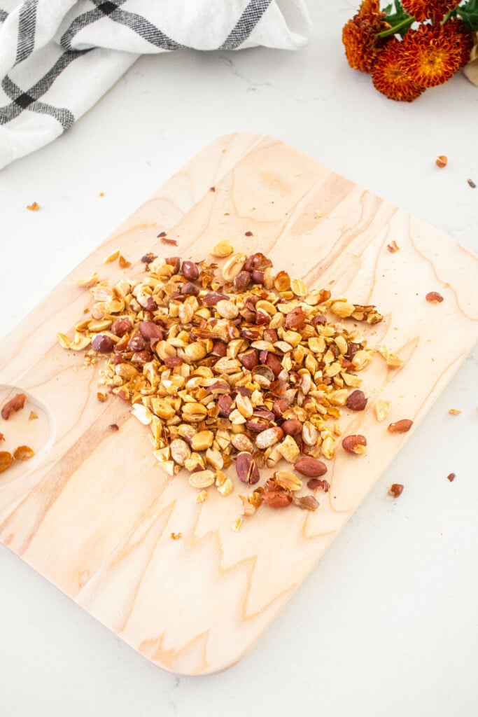 wood cutting board with chopped peanuts on a marble countertop.