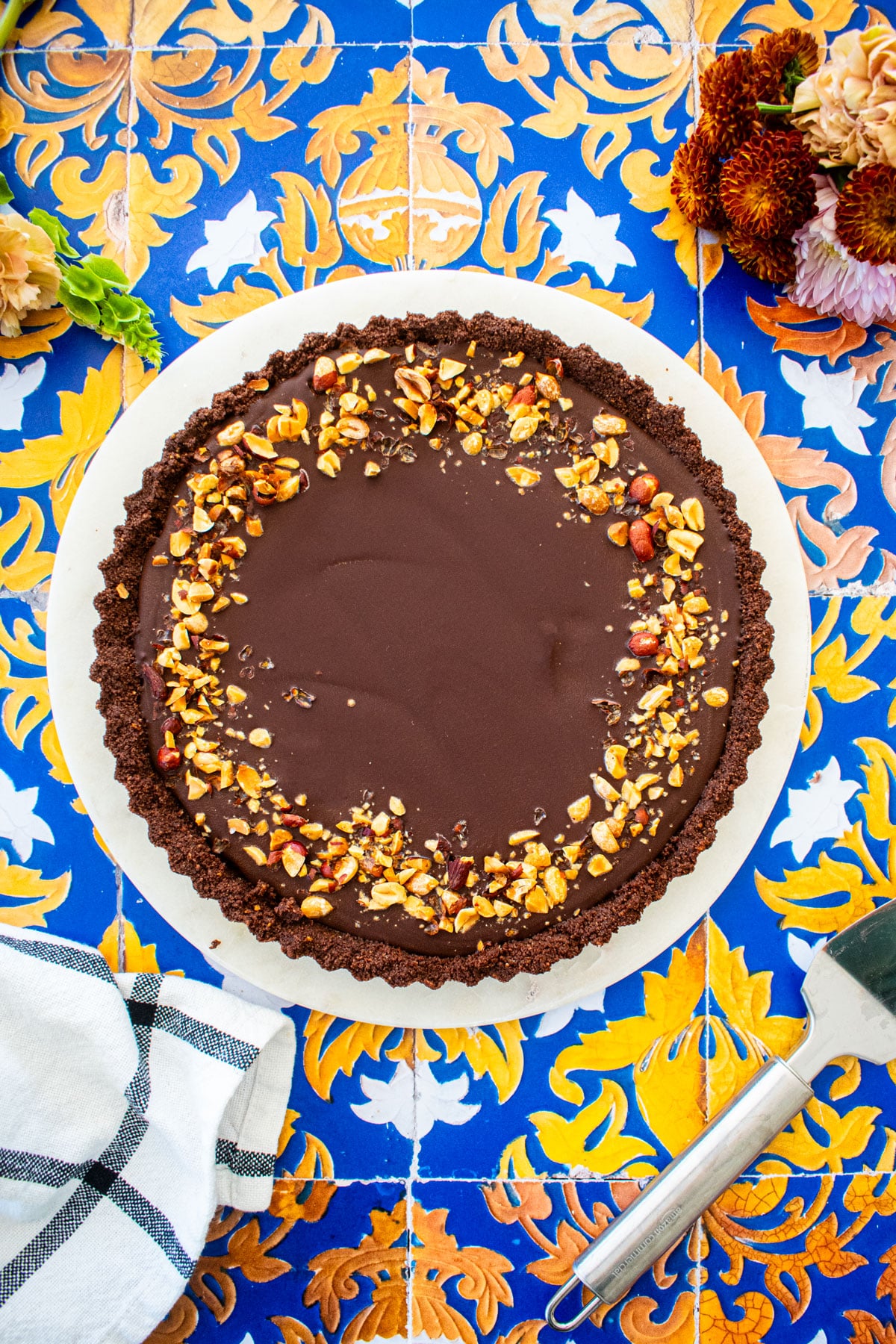chocolate peanut butter tart on a marble serving board on a tile table with fresh flowers.