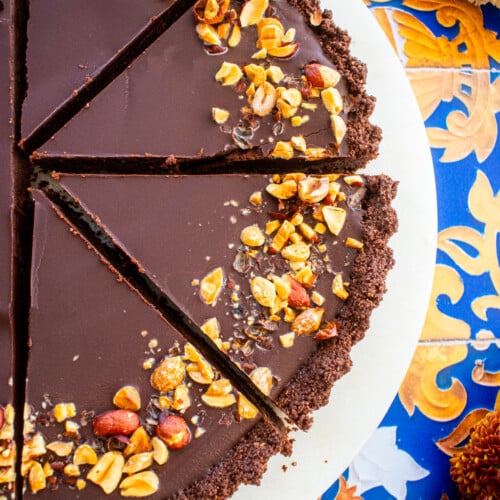 chocolate peanut butter tart sliced into slices on a marble serving board on a tile table with fresh flowers.