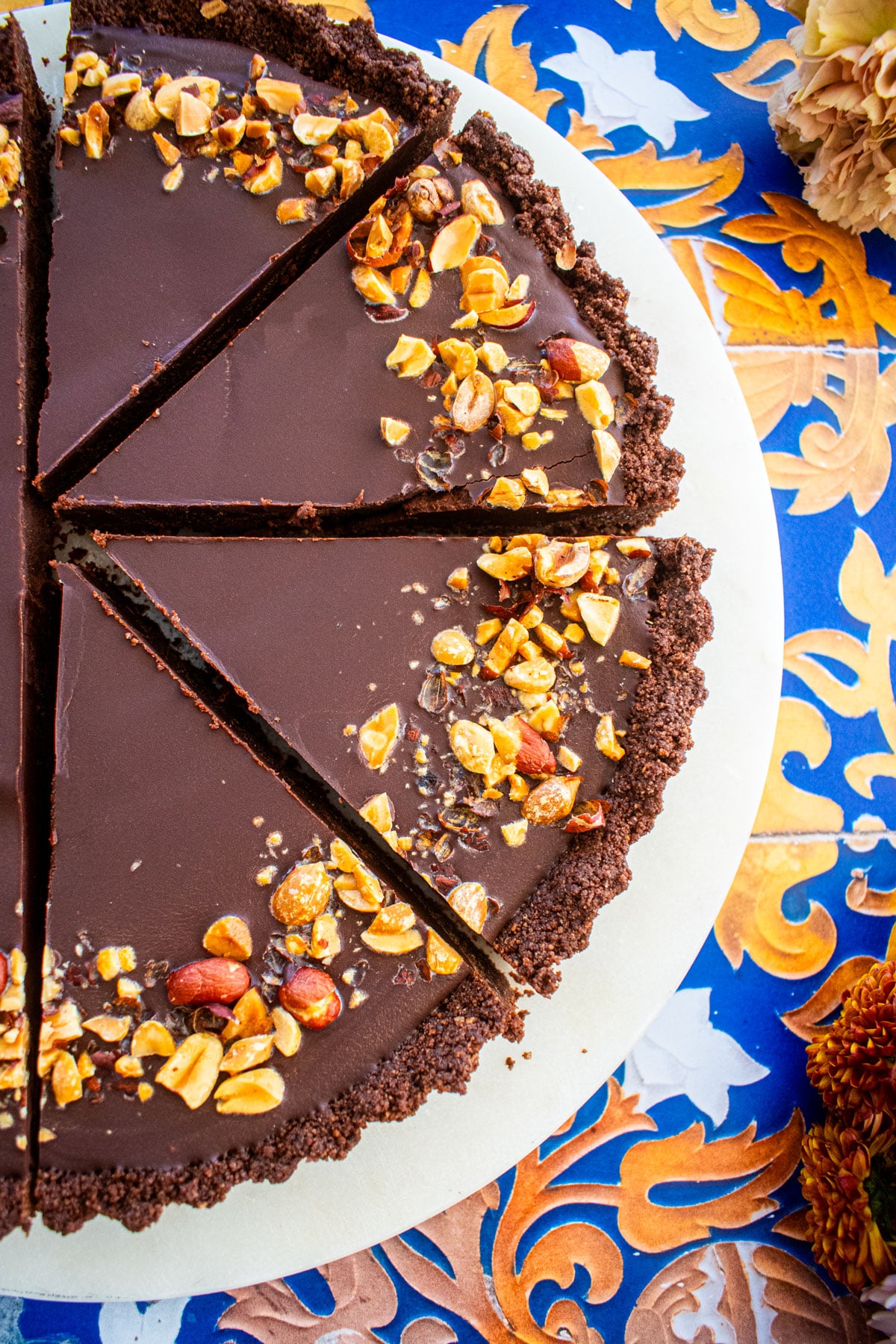 chocolate peanut butter tart sliced into slices on a marble serving board on a tile table with fresh flowers.