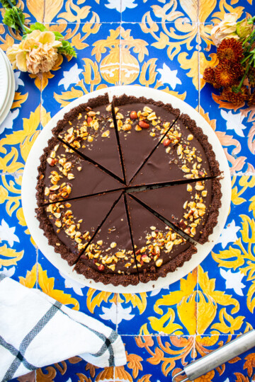 chocolate peanut butter tart sliced into slices on a marble serving board on a tile table with fresh flowers.
