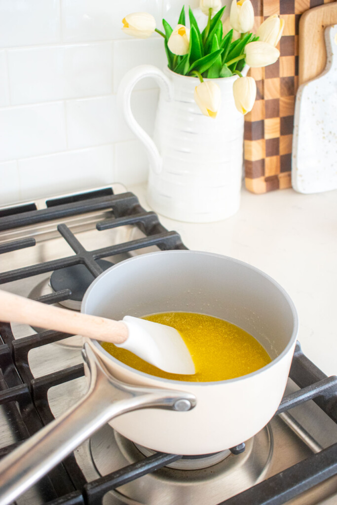 small pot on the stovetop with melted butter being stirred with a spatula.