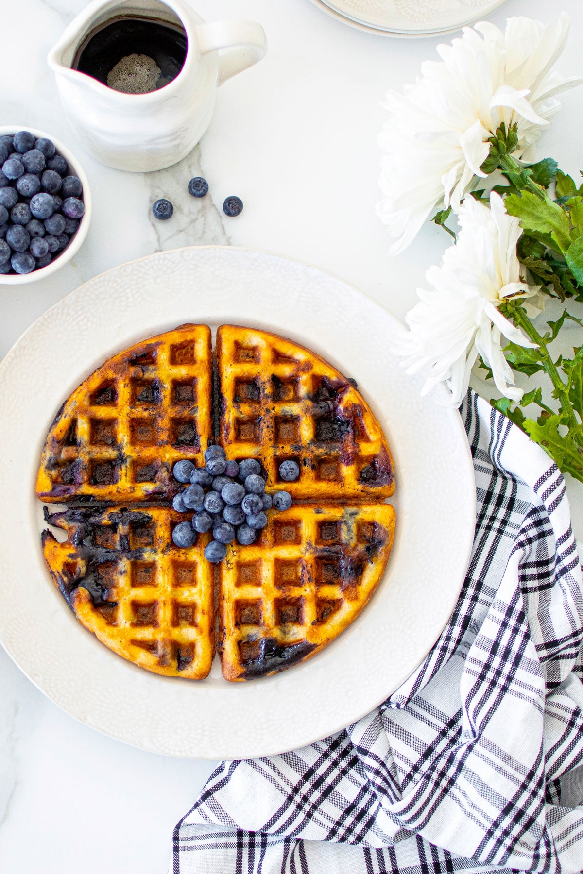 homemade blueberry waffles without eggs on a plate on a white marble counter with fresh blueberries and maple syrup.