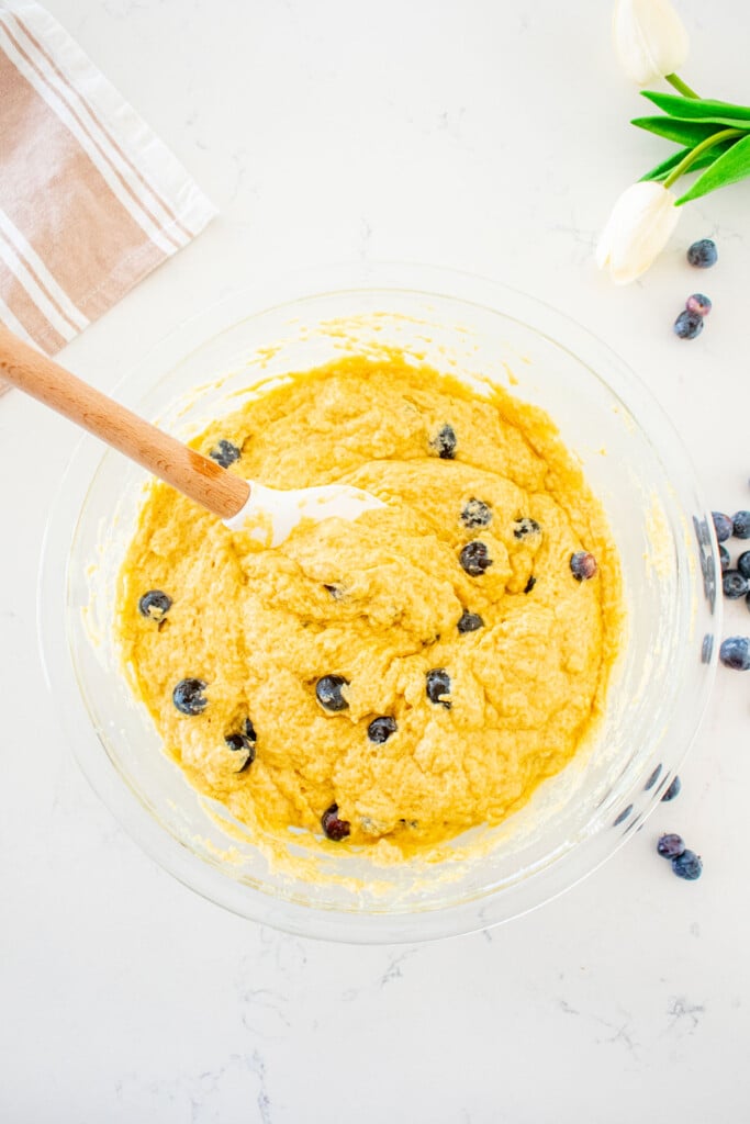 eggless blueberry waffle batter in a glass mixing bowl with a spatula on a white marble counter.