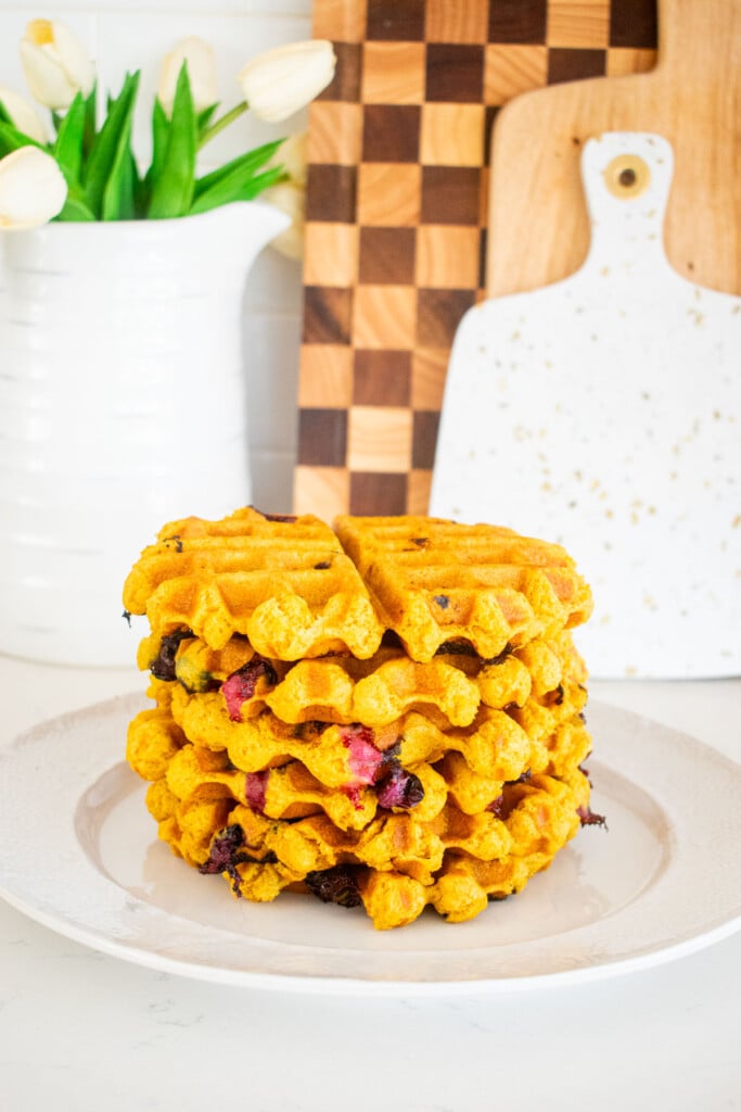 big stack of eggless blueberry waffles on a plate on a white marble counter.