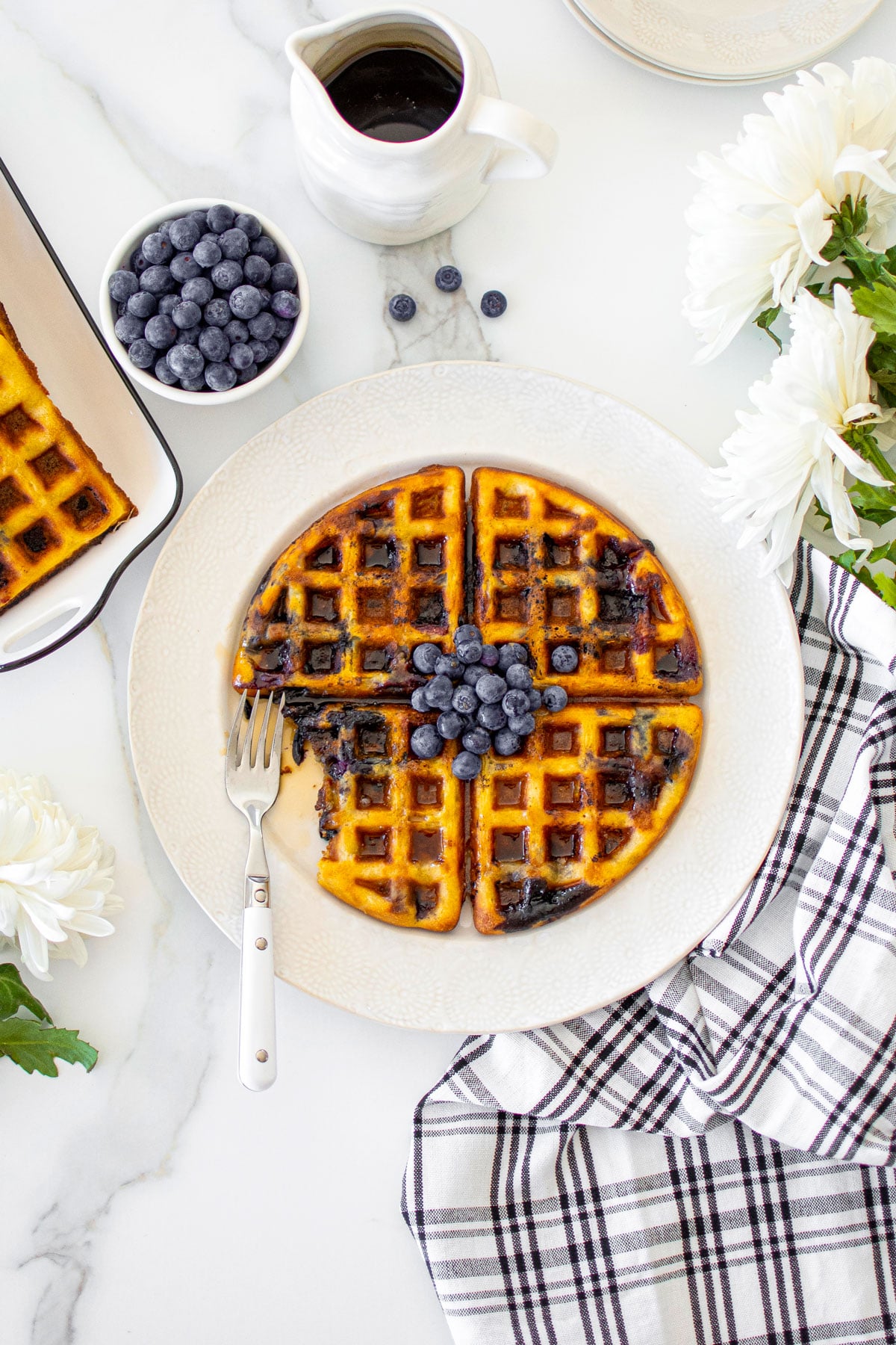 homemade blueberry waffles without eggs on a plate on a white marble counter with fresh blueberries and maple syrup.