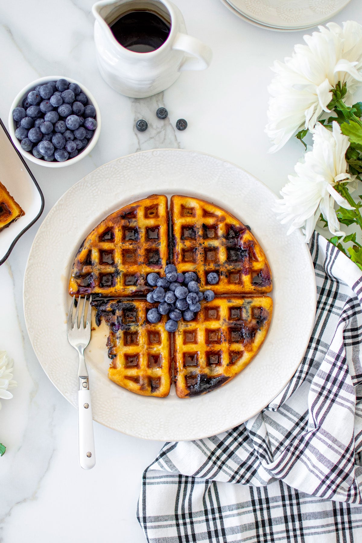 homemade blueberry waffles without eggs on a plate on a white marble counter with fresh blueberries and maple syrup.