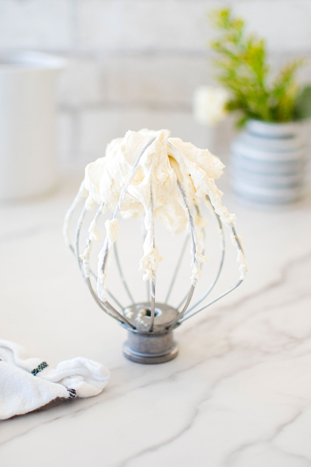 homemade organic whipped cream on a whisk on a white marble counter.