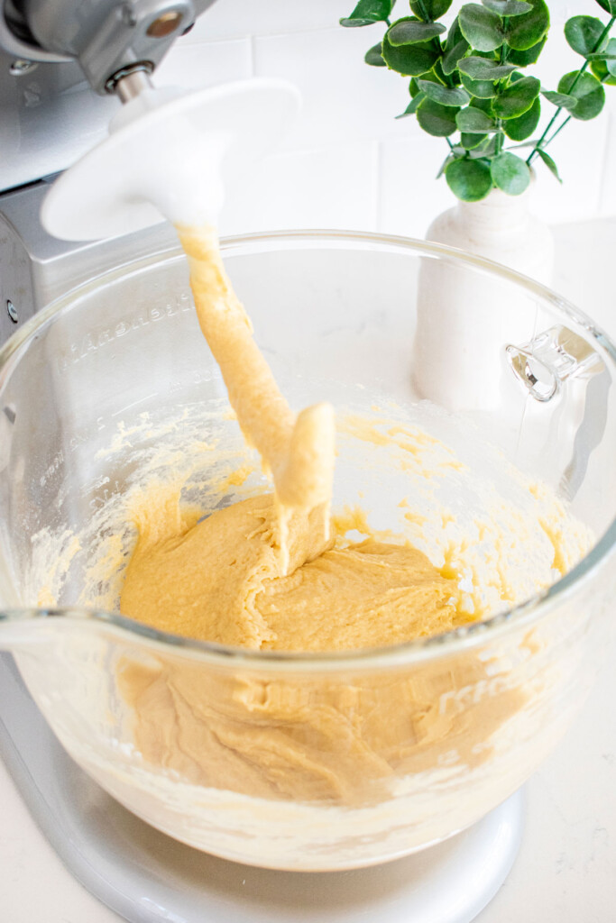 organic brioche bun dough in a glass mixing bowl on a white kitchen counter.