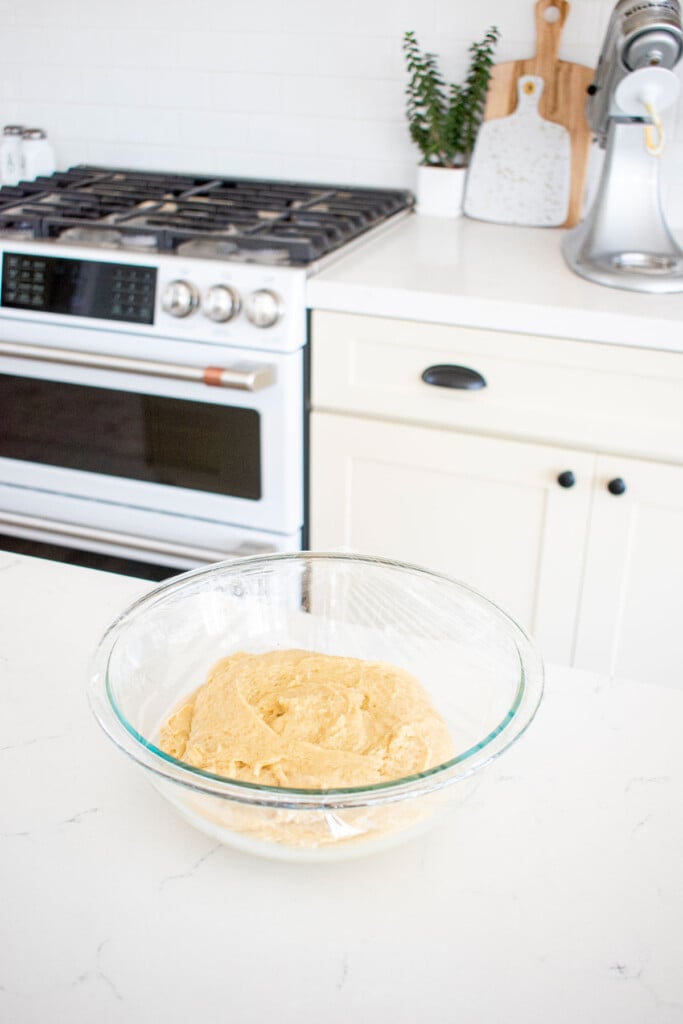 organic brioche bun dough in a glass mixing bowl on a white kitchen counter.
