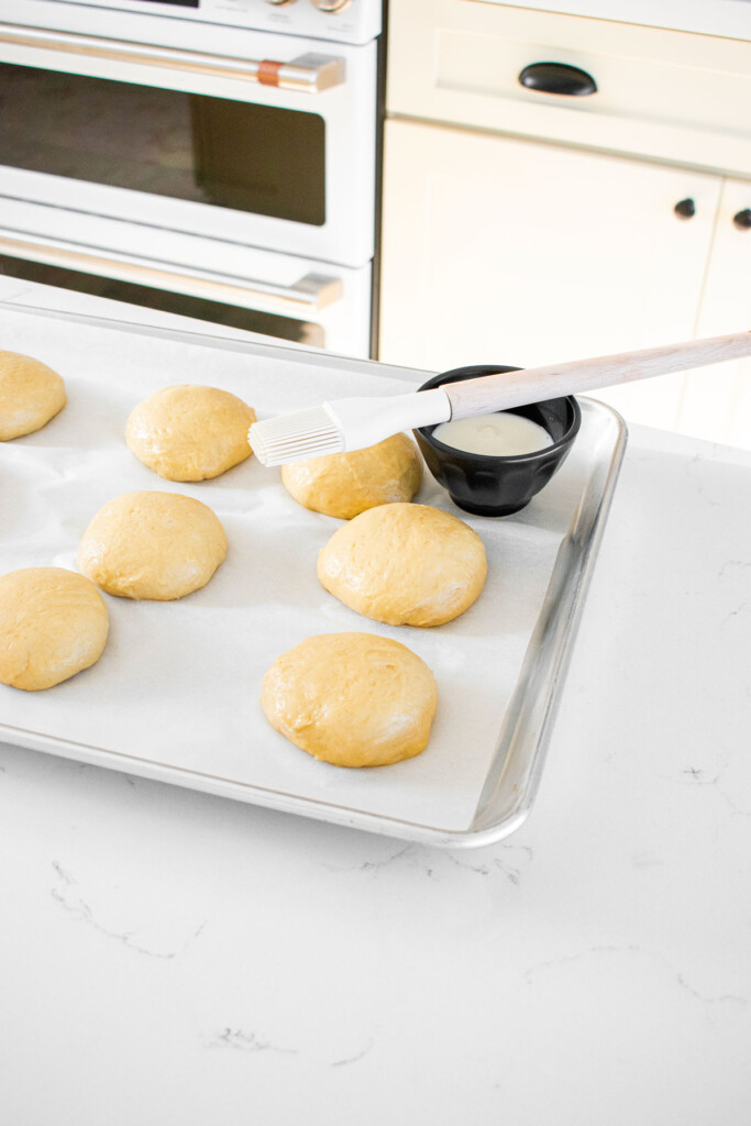 brioche buns dough on a baking sheet being brushed with milk.