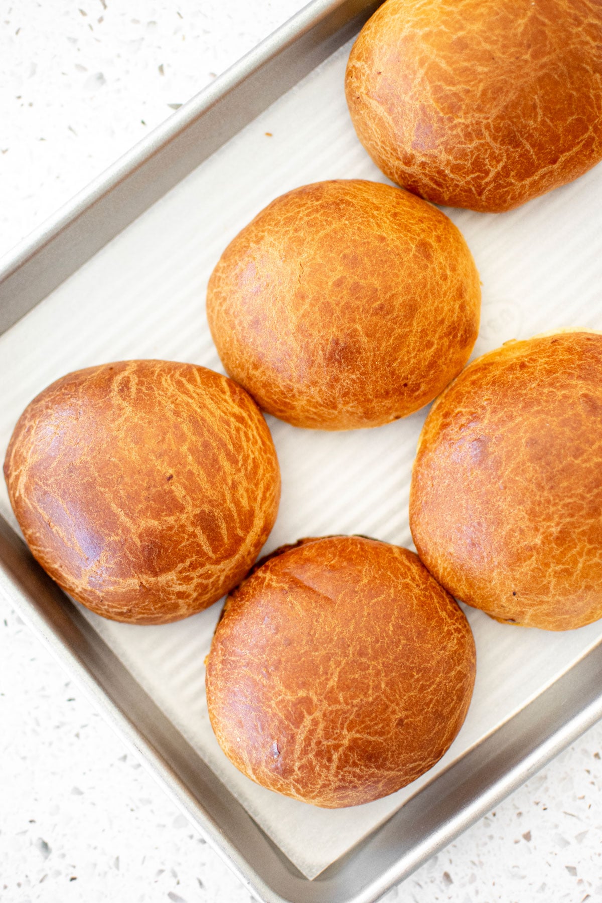 organic brioche buns with instant yeast on a baking sheet on a white stone counter.