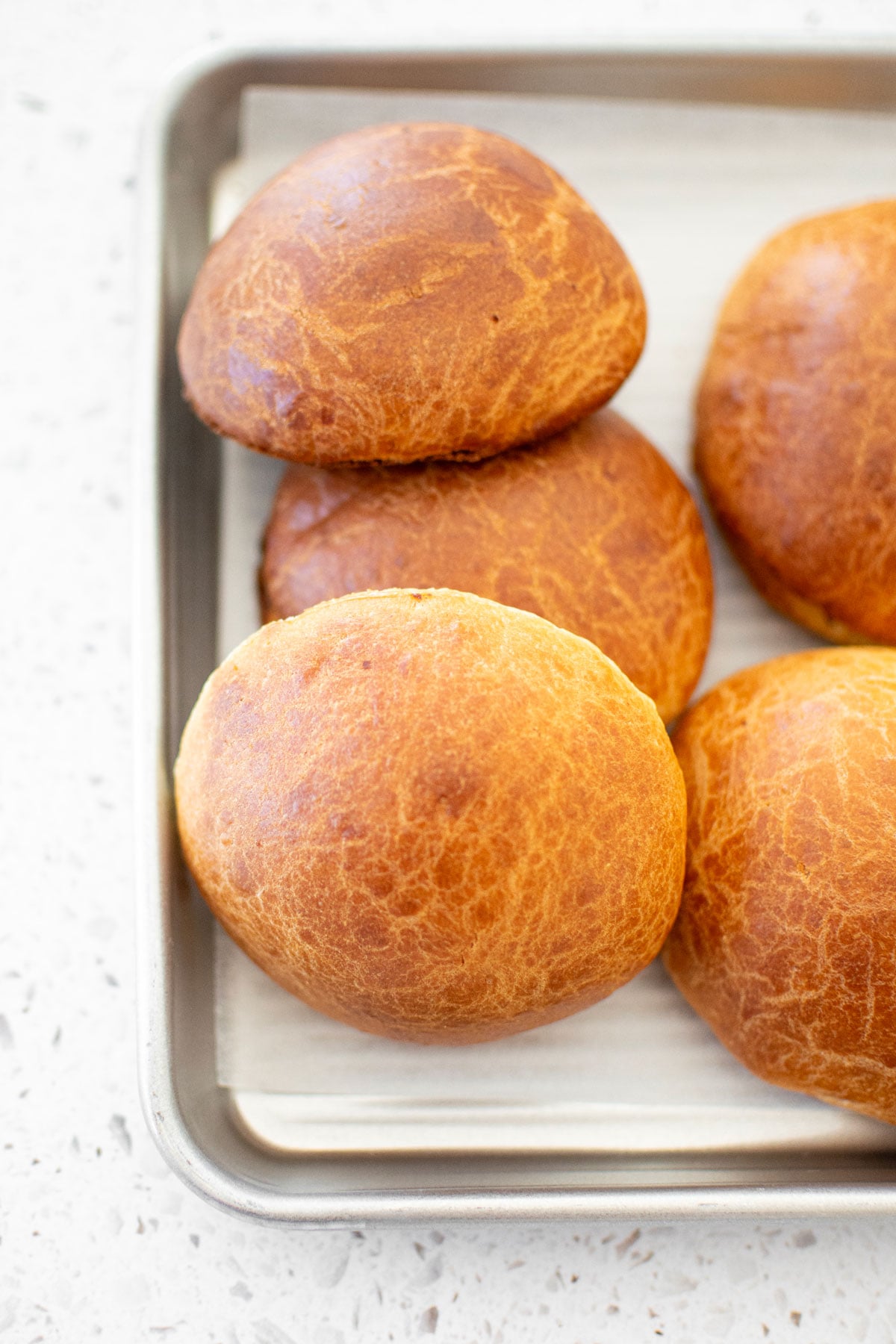 organic brioche buns with instant yeast on a baking sheet on a white stone counter.