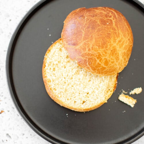 brioche bun cut in half on a black plate on a white stone counter.