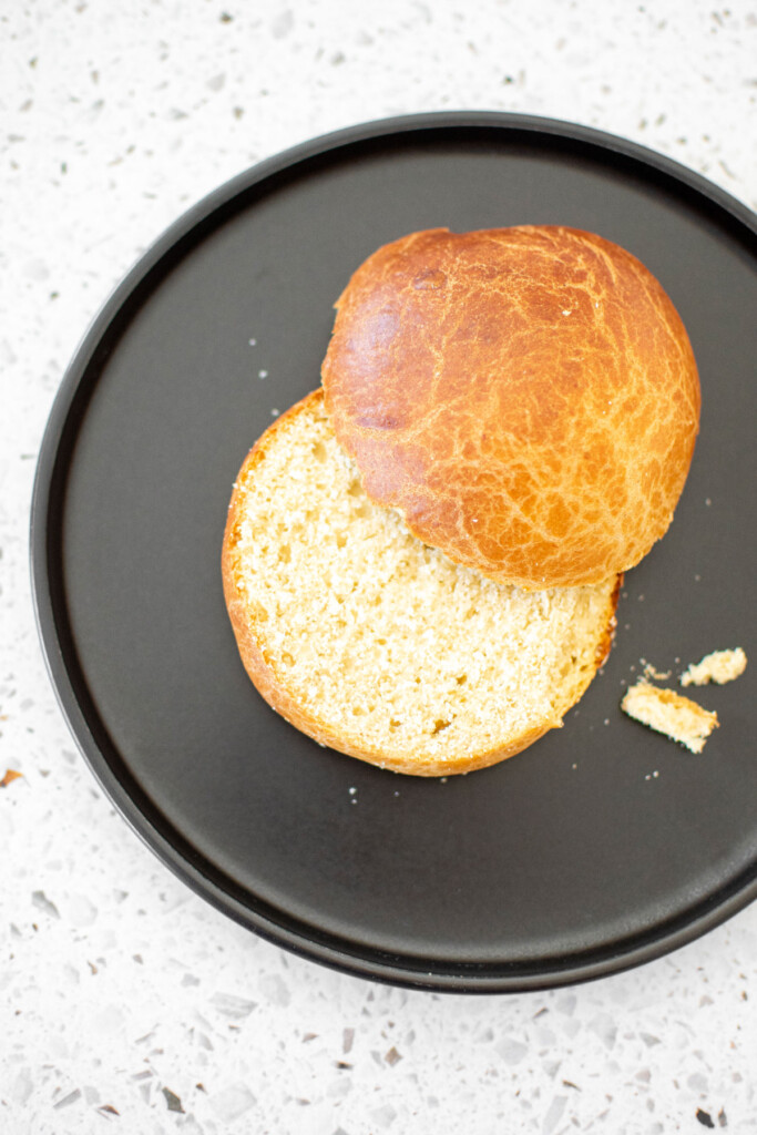 brioche bun cut in half on a black plate on a white stone counter.