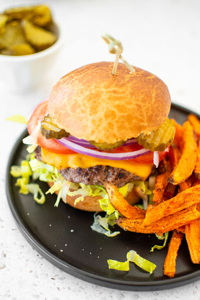cheeseburger on a brioche bun on a black plate with sweet potato fries.