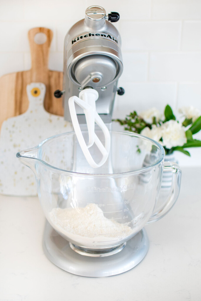 flour for pie crust in a stand mixing bowl on a marble counter with a vase of fresh flowers.