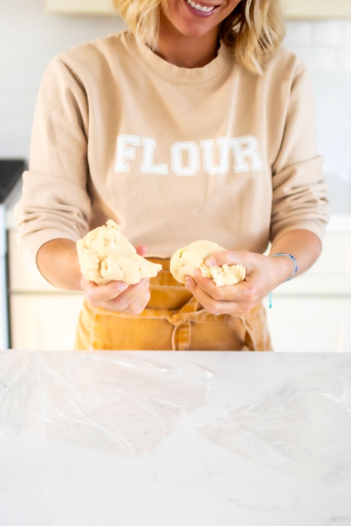 woman dividing pie dough in half wearing a flour sweatshirt and apron.