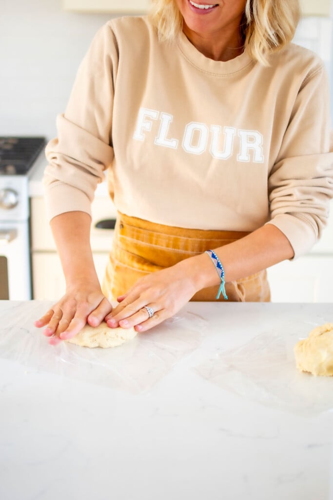 woman forming pie crust at kitchen counter wearing a flour sweatshirt and apron.