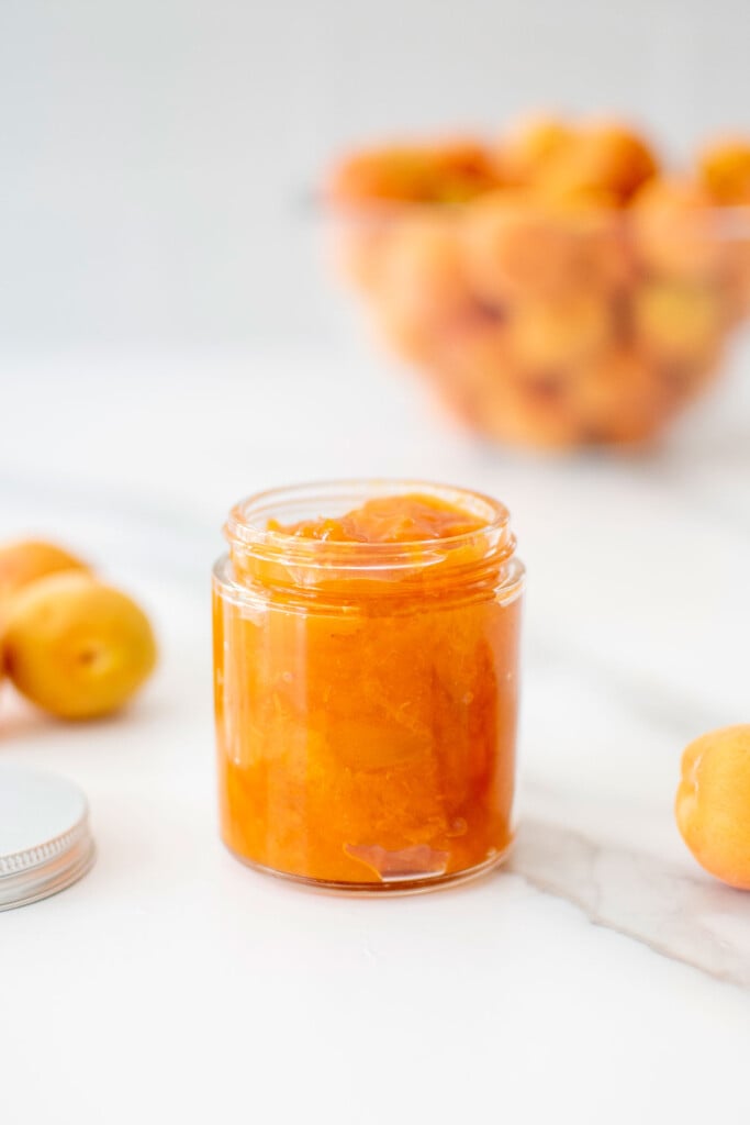 glass jar of apricot jam on a white marble counter.