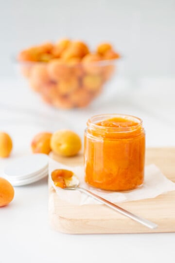 organic apricot jam in a glass jar on a wood cutting board on a marble counter.