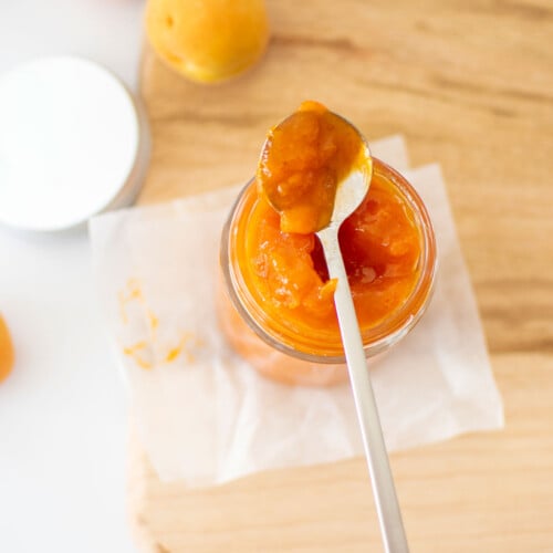 organic apricot jam in a glass jar on a wood cutting board on a marble counter.